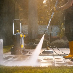 A Person Power Washing a Patio With a Pressure Washer in a Sunny Outdoor Setting
